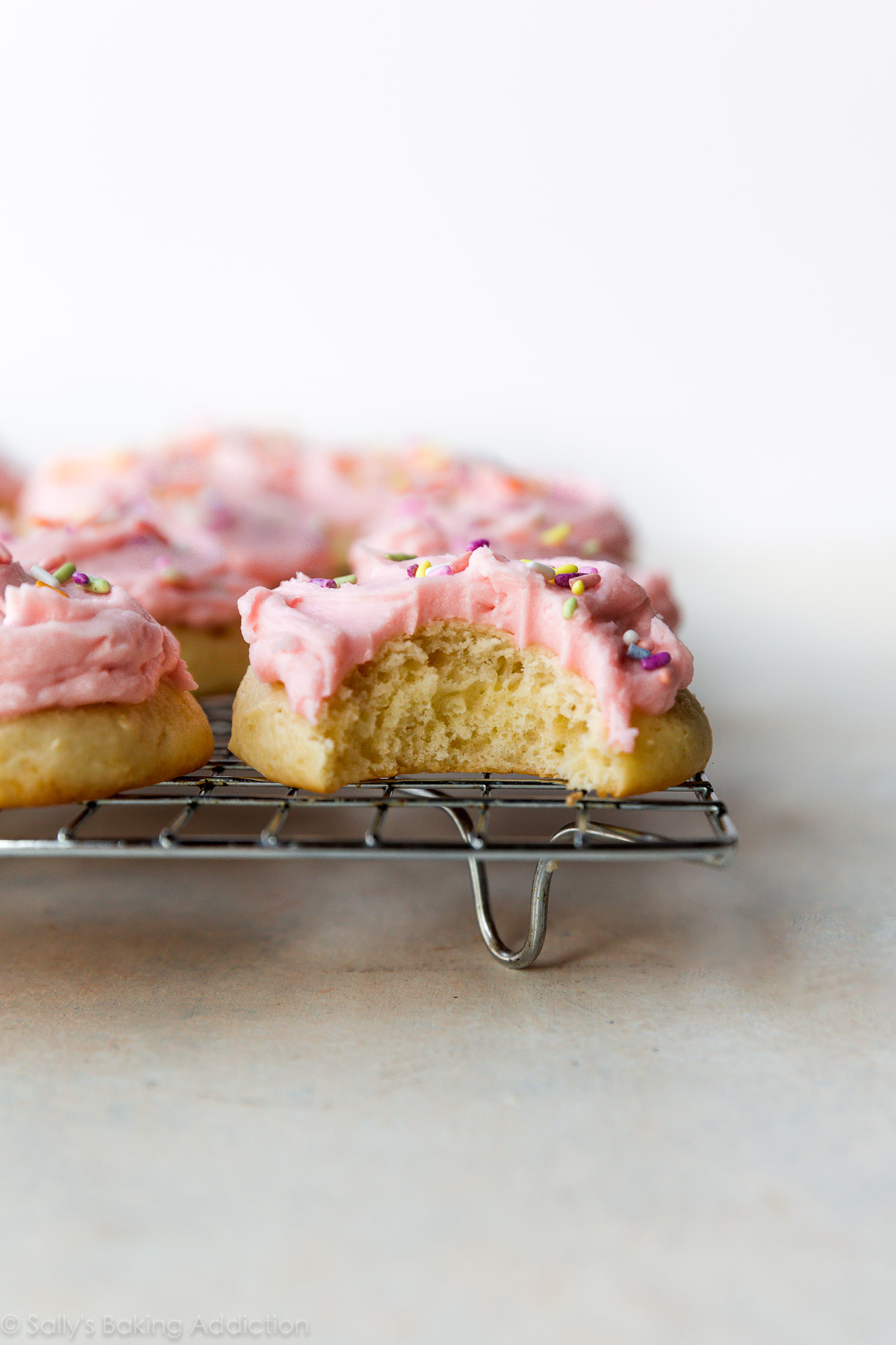 Ces biscuits sucrés en forme de gâteau sont garnis de crème au beurre rose pastel crémeuse et de paillettes. La crème sure est l'ingrédient secret! Recette sur sallysbakingaddiction.com
