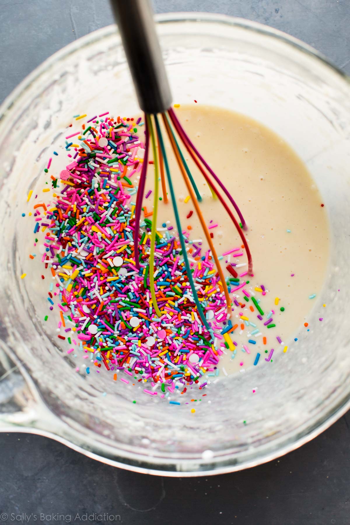 pâte à cupcake funfetti dans un bol en verre avec un fouet de couleur arc-en-ciel