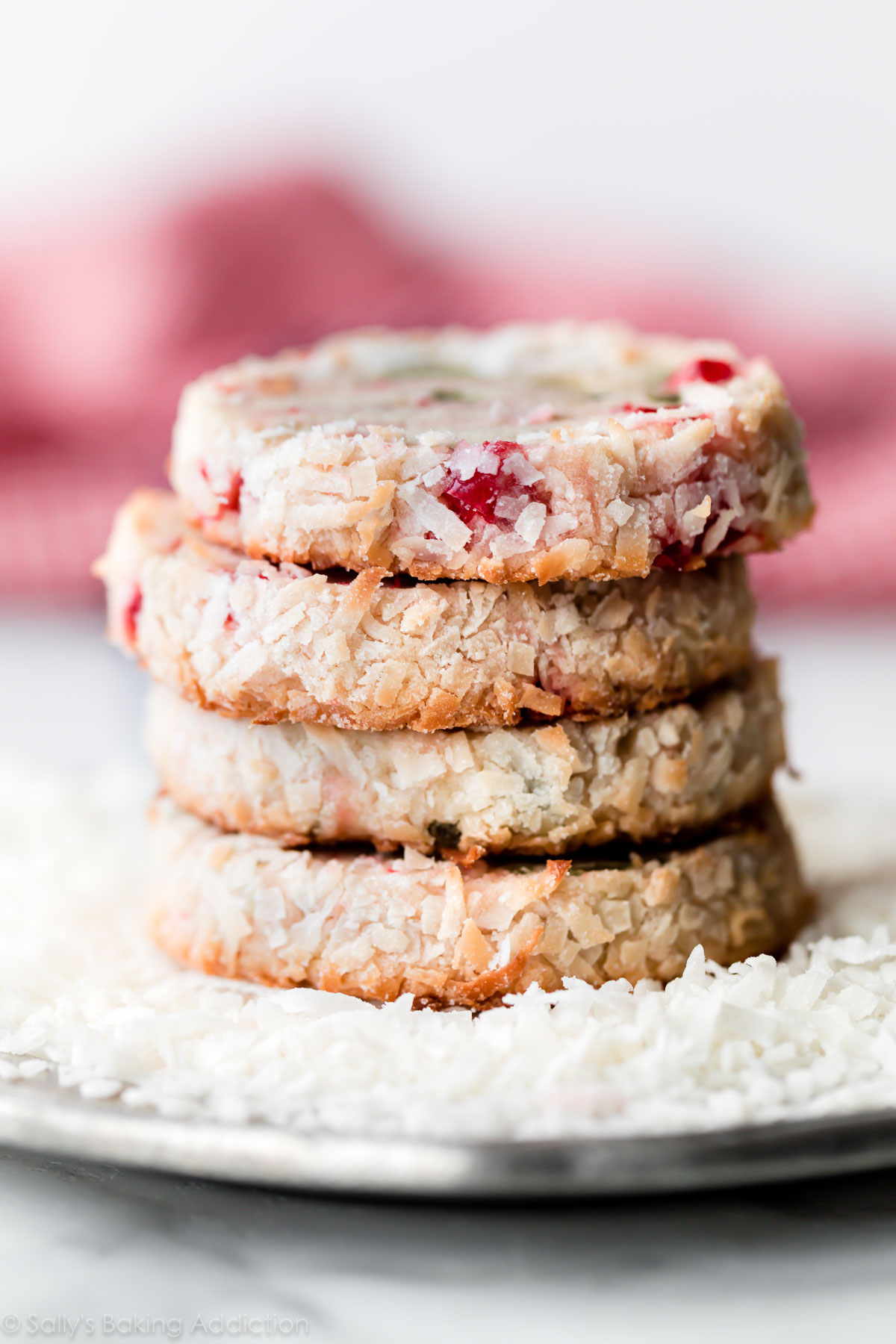 Les biscuits du Père Noël sont des biscuits au beurre tranchés et cuits avec des cerises douces, une saveur d'amande, et sont roulés dans de la noix de coco. Recette sur sallysbakingaddiction.com