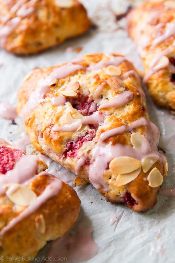 Scones feuilletés, doux et tendres avec des framboises juteuses et une saveur d'amande à chaque bouchée. Prenez tous mes conseils de cuisson au scone et la recette sur sallysbakingaddiction.com