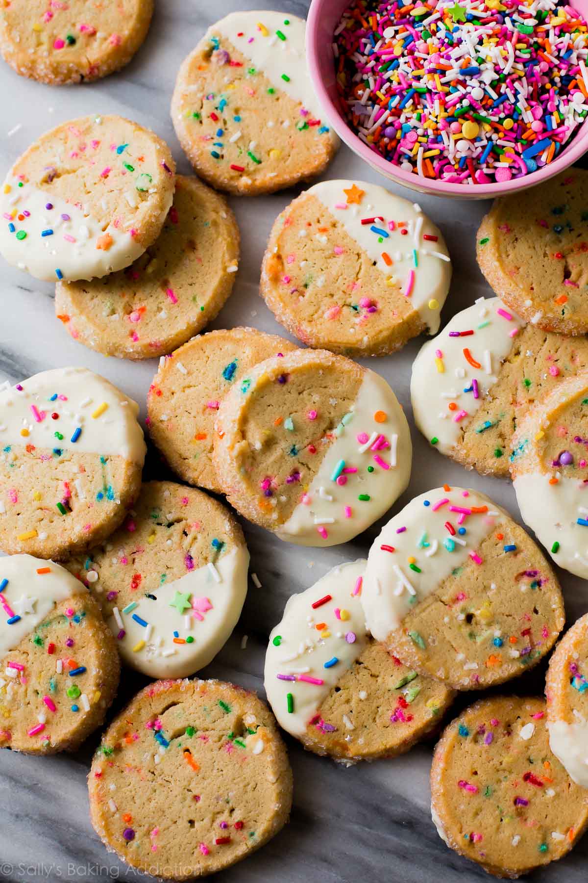 image aérienne d'une tranche de funfetti et de biscuits cuits au four avec la moitié de chaque biscuit trempé dans du chocolat blanc et garni de vermicelles