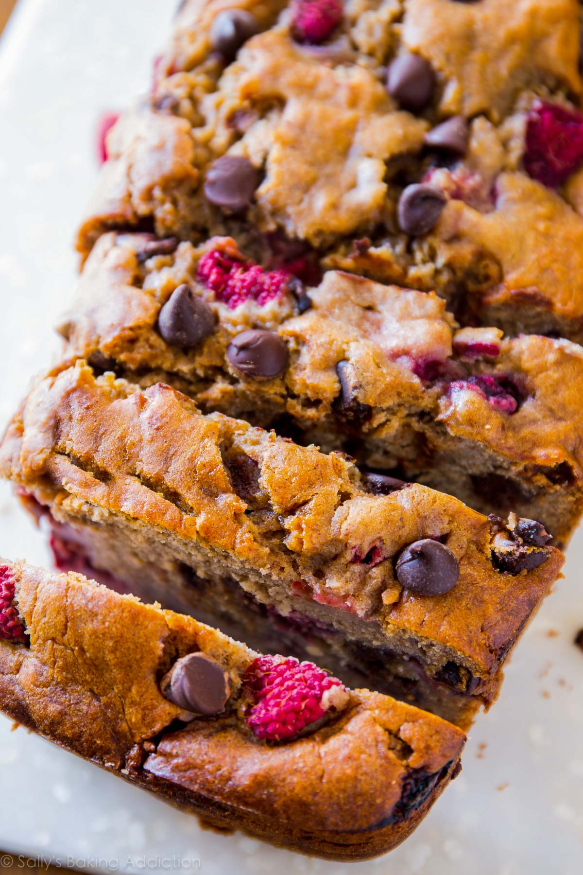 Pain aux bananes au sucre brun super moelleux et incroyablement gourmand avec des framboises juteuses et des pépites de chocolat noir. Ma recette de pain aux bananes préférée! sallysbakingaddiction.com