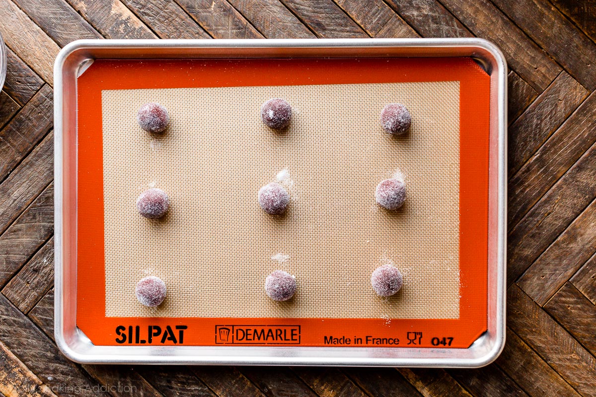 Boules de pâte à biscuits de velours rouge roulées dans du sucre disposées sur une plaque à pâtisserie