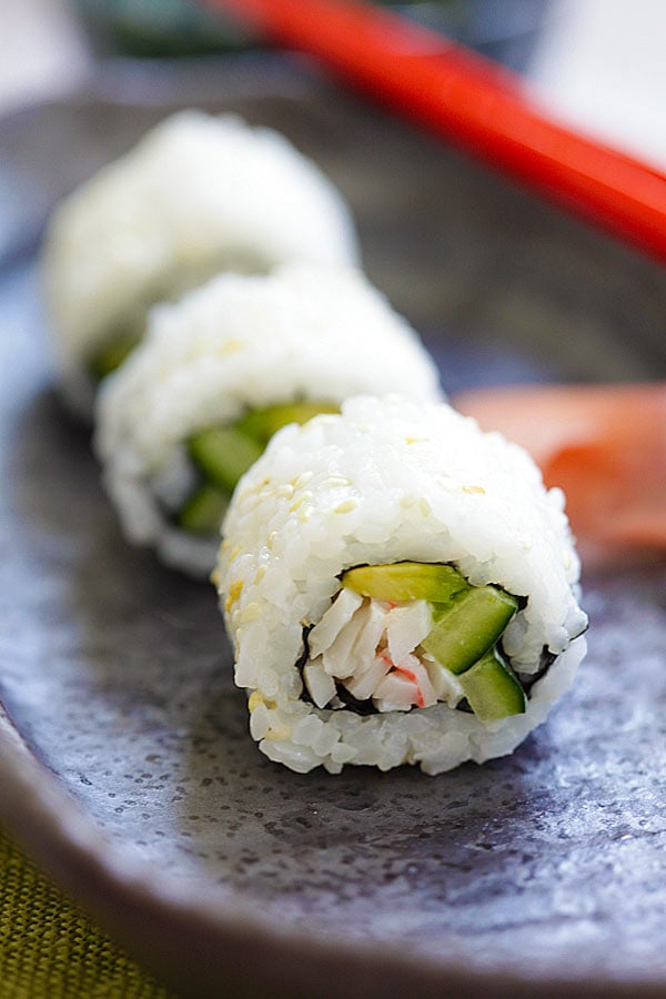 Une recette de sushi California roll coupée en 3 morceaux, prête à servir avec des baguettes.