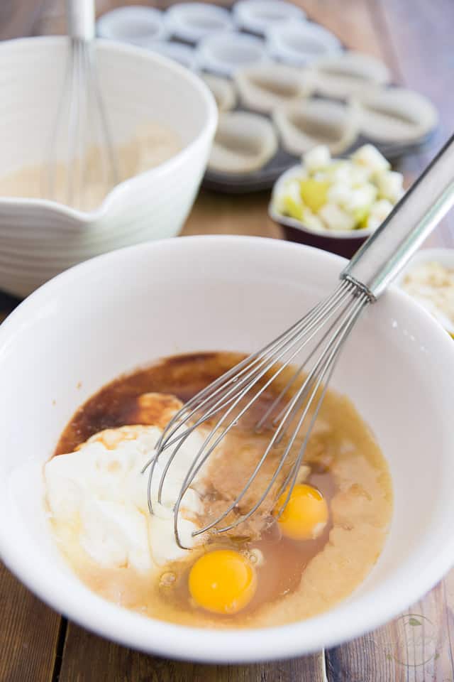 Œufs, yogourt, purée de poire, miel et extrait de vanille dans un bol en céramique blanche avec un fouet dépassant du côté droit