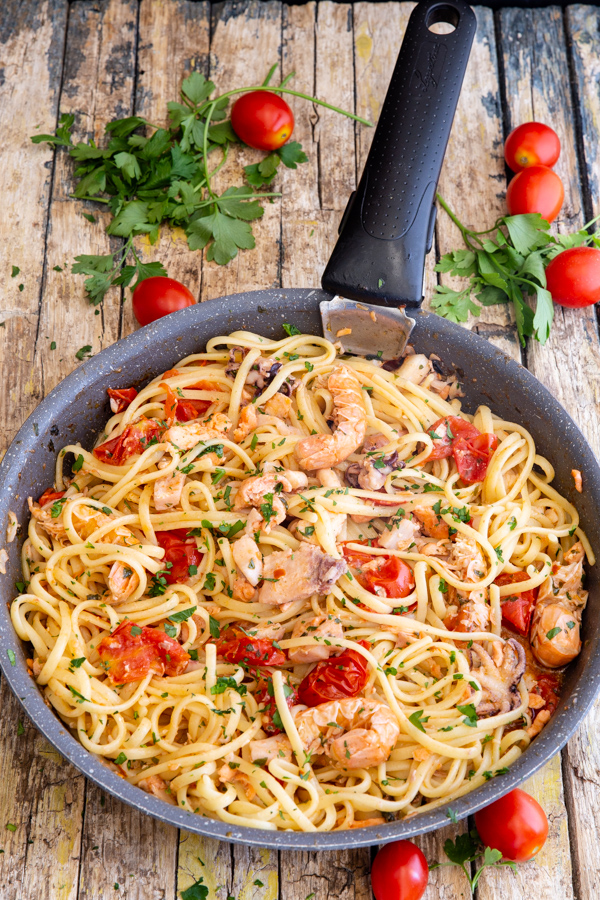 pâtes aux fruits de mer dans une poêle noire, avec des tomates raisins autour.