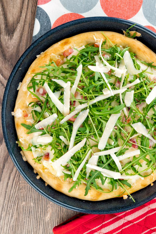 Pizza blanche avec roquette et flocons de parmesan sur une plaque à pizza noire.