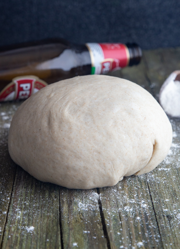 Pâte à pizza à la bière sur une planche avec une bouteille de bière derrière.