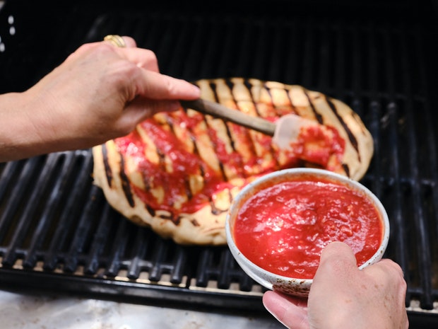 Étendre la sauce tomate sur la pâte à pizza” border=