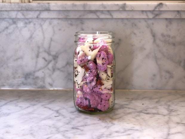 Vue latérale d'un pot rempli de bouquets de chou-fleur, d'oignons, de graines de moutarde et de piments