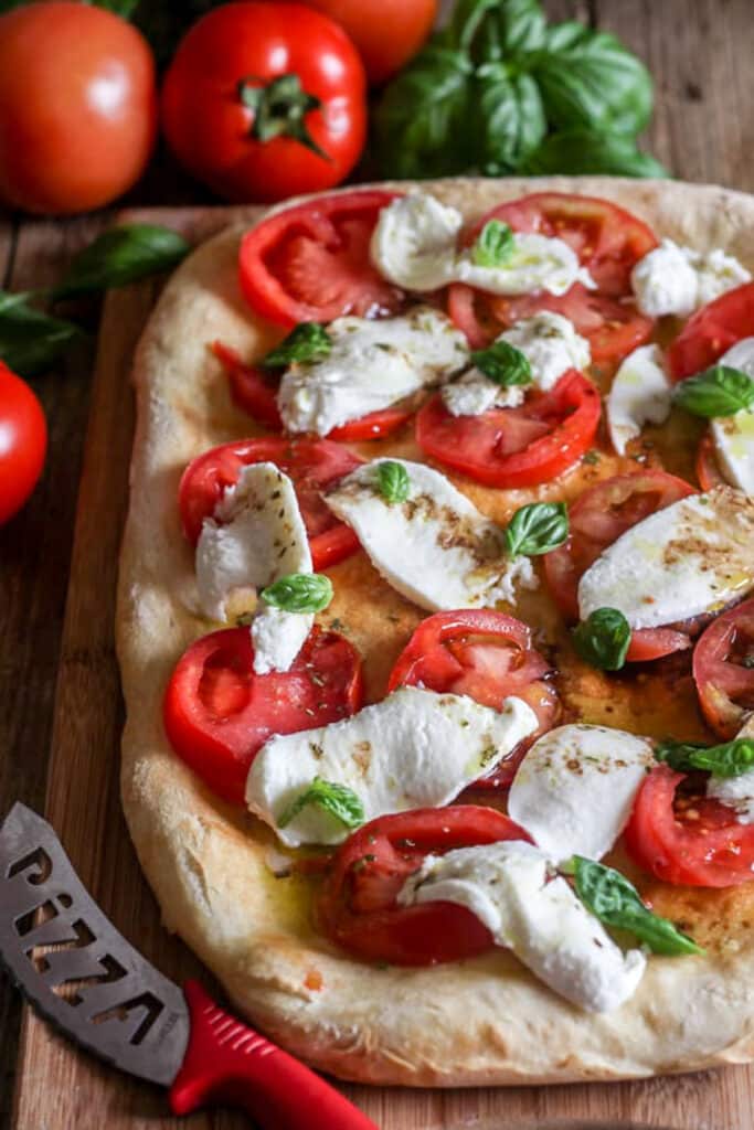 Pizza sur une planche avec des tomates et un couteau rouge.