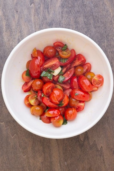 Tomates, basilic, ail, huile d'olive dans un bol blanc.