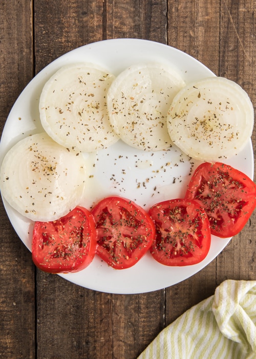 Les oignons tranchés et les tomates préparés sur une assiette blanche.